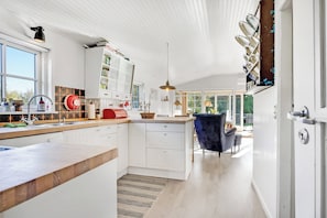 A modern kitchen with white cabinetry, a wooden countertop, and a view into the dining area. - Lovely cottage in Hals 250 m to the beach (Hals)