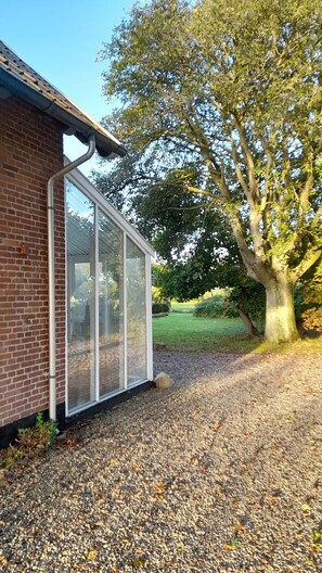 Ein Haus mit Backsteinfassade, einem großen Fenster und einer Auffahrt mit Kies, die zu einem Baum führt.