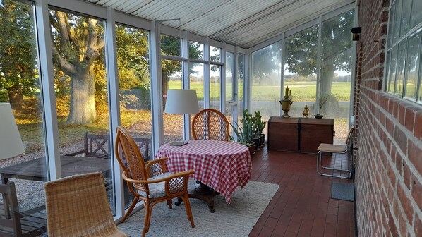 Eine überdachte Terrasse mit Tisch, Stühlen, einer Lampe, einer Zierkiste und Blick ins Freie.