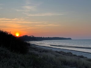 Une plage au coucher du soleil, avec un ciel dégagé, une mer calme et une terre lointaine à l’horizon.