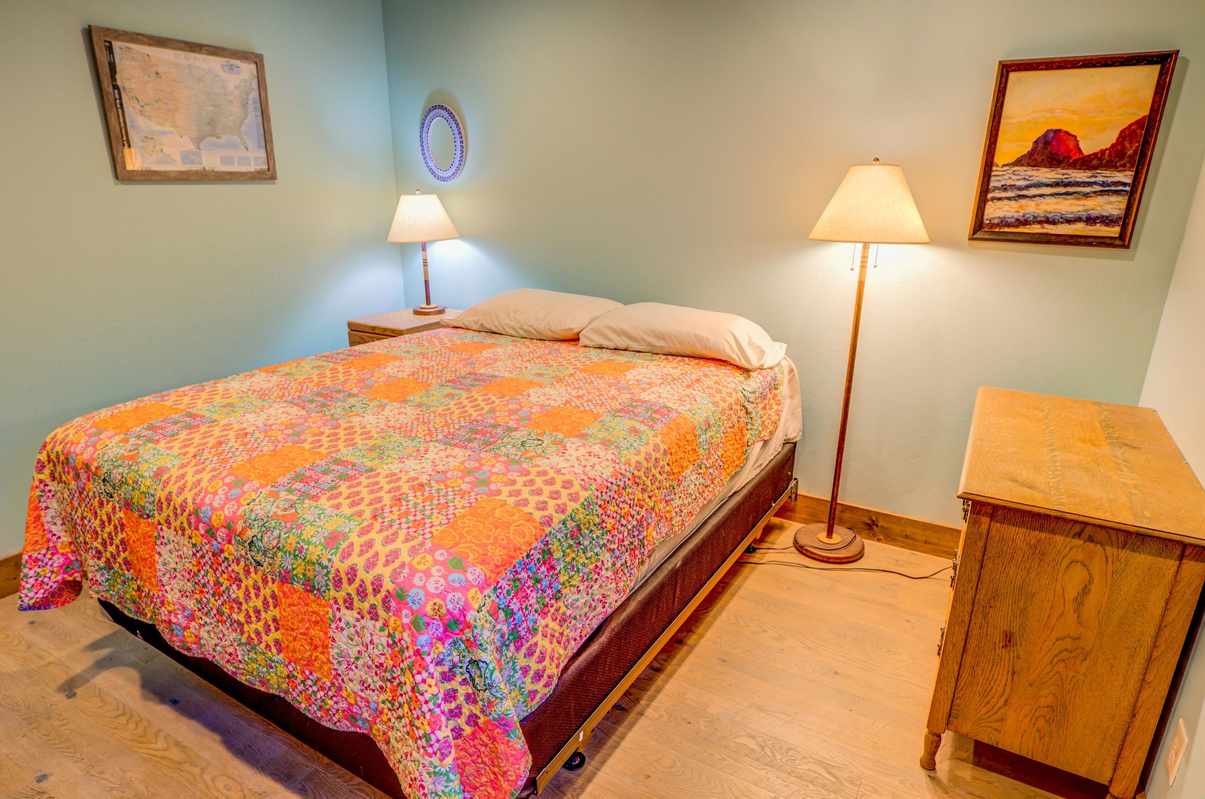 Ein Schlafzimmer mit einem farbenfrohen Quilt, einem Holznachttisch, einem Schreibtisch und zwei Wandlampen.