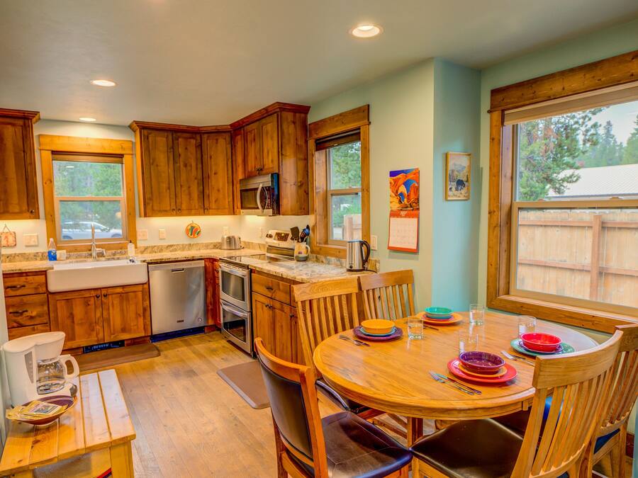 Una cocina con armarios de madera, una mesa de comedor con sillas y una ventana con vistas a una valla de madera.