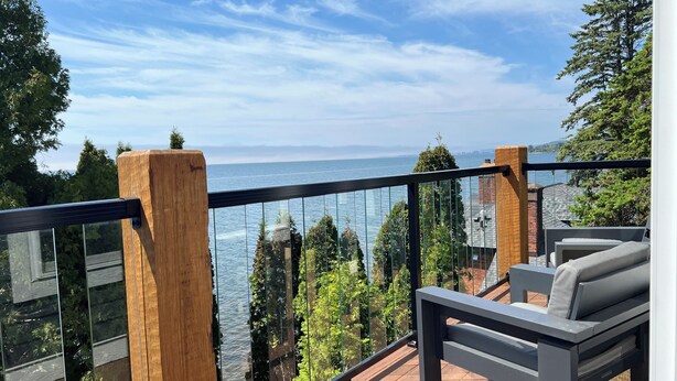 Un balcon doté d’une balustrade en verre donnant sur une étendue d’eau, avec des poteaux en bois et des meubles d’extérieur.