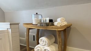 Une étagère en bois avec des serviettes et des articles de toilette, dans une pièce dotée de meubles blancs et d’un plancher en bois.