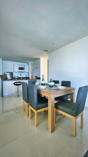 Una cocina moderna con microondas, lavaplatos y armarios. Hay una zona de comedor con una mesa y sillas de madera.