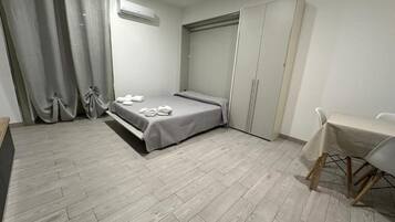 Ein Schlafzimmer mit einem Bett, einem Schreibtisch, einem Stuhl, einem Kleiderschrank und einem Vorhang.