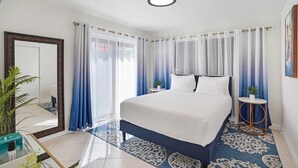 Une chambre avec un grand lit, une table de chevet, un miroir et une vue sur l’extérieur.