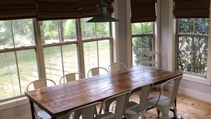 A dining area with a wooden table and white chairs, large windows with blinds, and a hanging light fixture. - Craftsman style family gathering home close to Guntersville (Scottsboro)