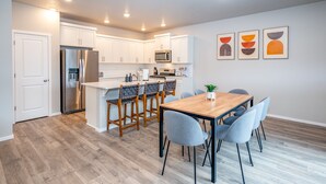 A modern kitchen with white cabinets, stainless steel appliances, and a wooden dining table with chairs.
