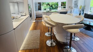 A modern kitchen with a central island, bar stools, and a view of a bedroom through an open door.