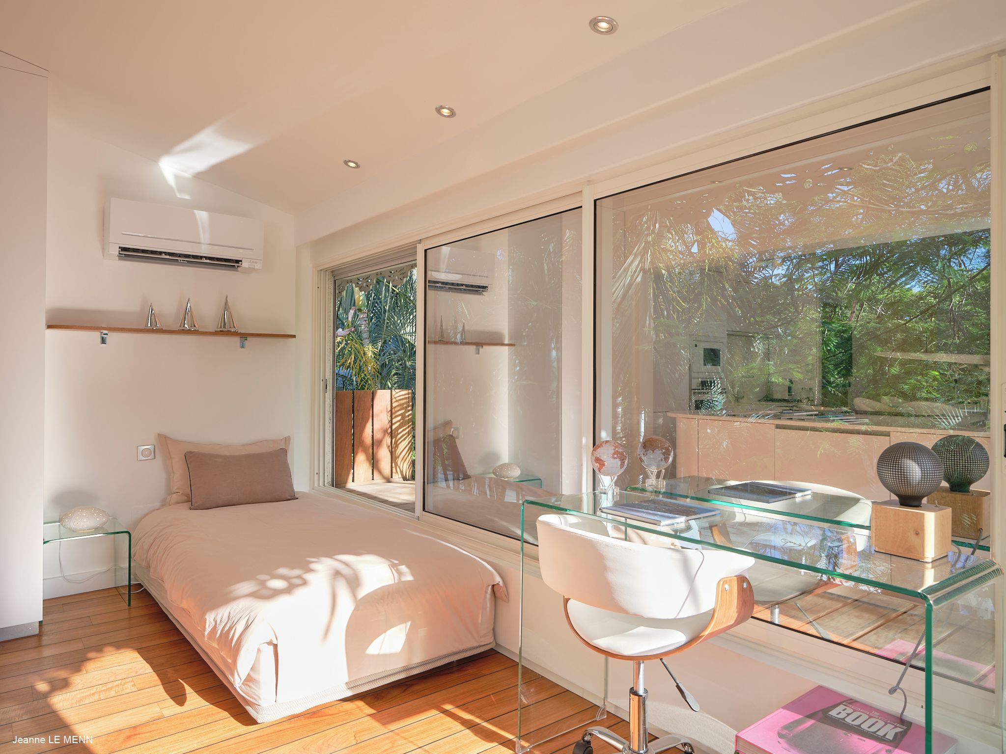 A modern bedroom with a glass desk, a bed, and a large window.