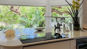 A modern kitchen with a large island, a view of lush greenery outside, and a ceiling with recessed lighting.