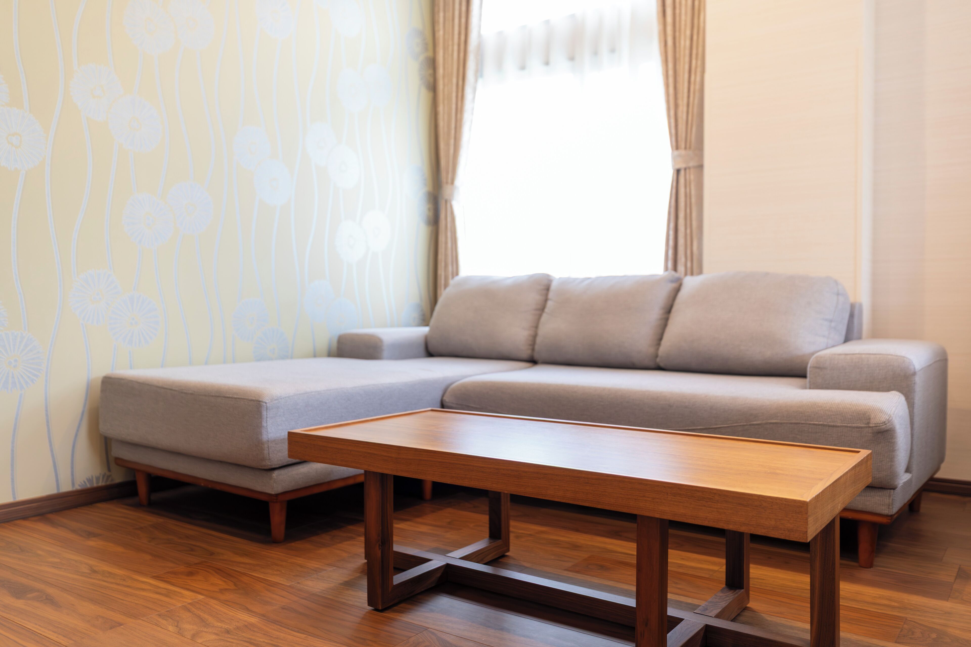Un salon moderne avec un canapé d’angle, une table basse en bois et un papier peint à motifs.