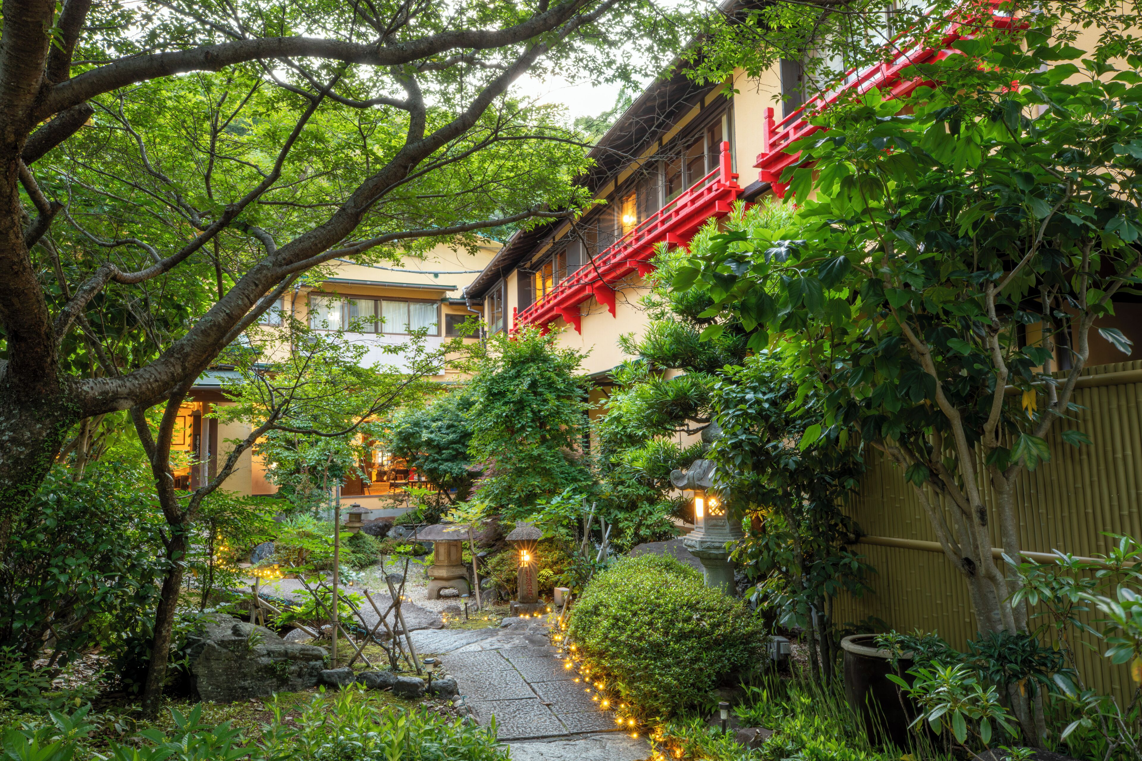 A traditional Japanese garden with a stone pathway, lanterns, and a building with red accents.