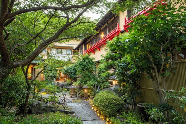 A traditional Japanese garden with a stone pathway, lanterns, and a building with red accents. - Koubounoyu Honten (Izunokuni)