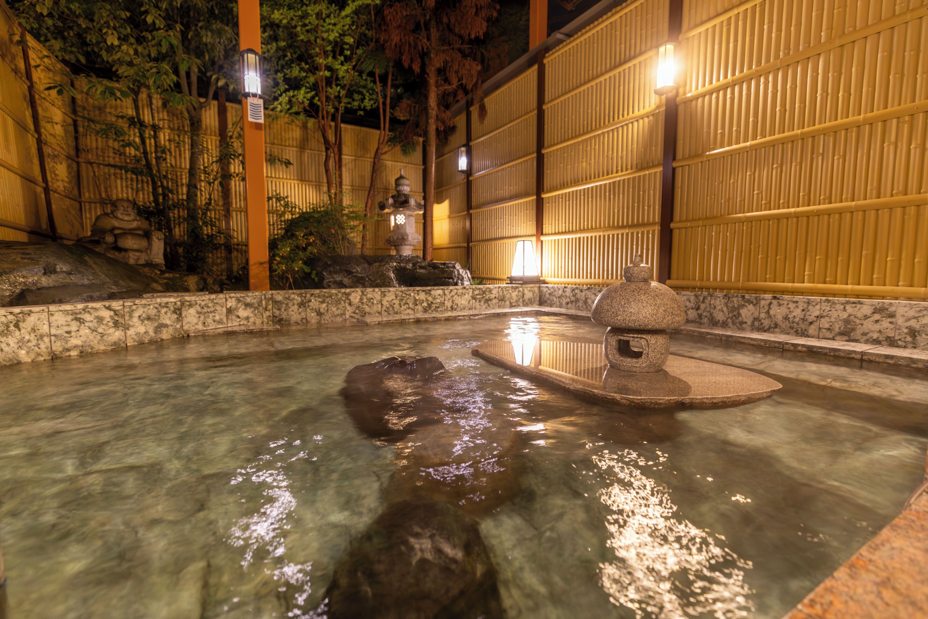 Ein traditionelles japanisches Onsen mit einem Steingrundschalenbad, Bambuswänden und einem kleinen Wasserfall.