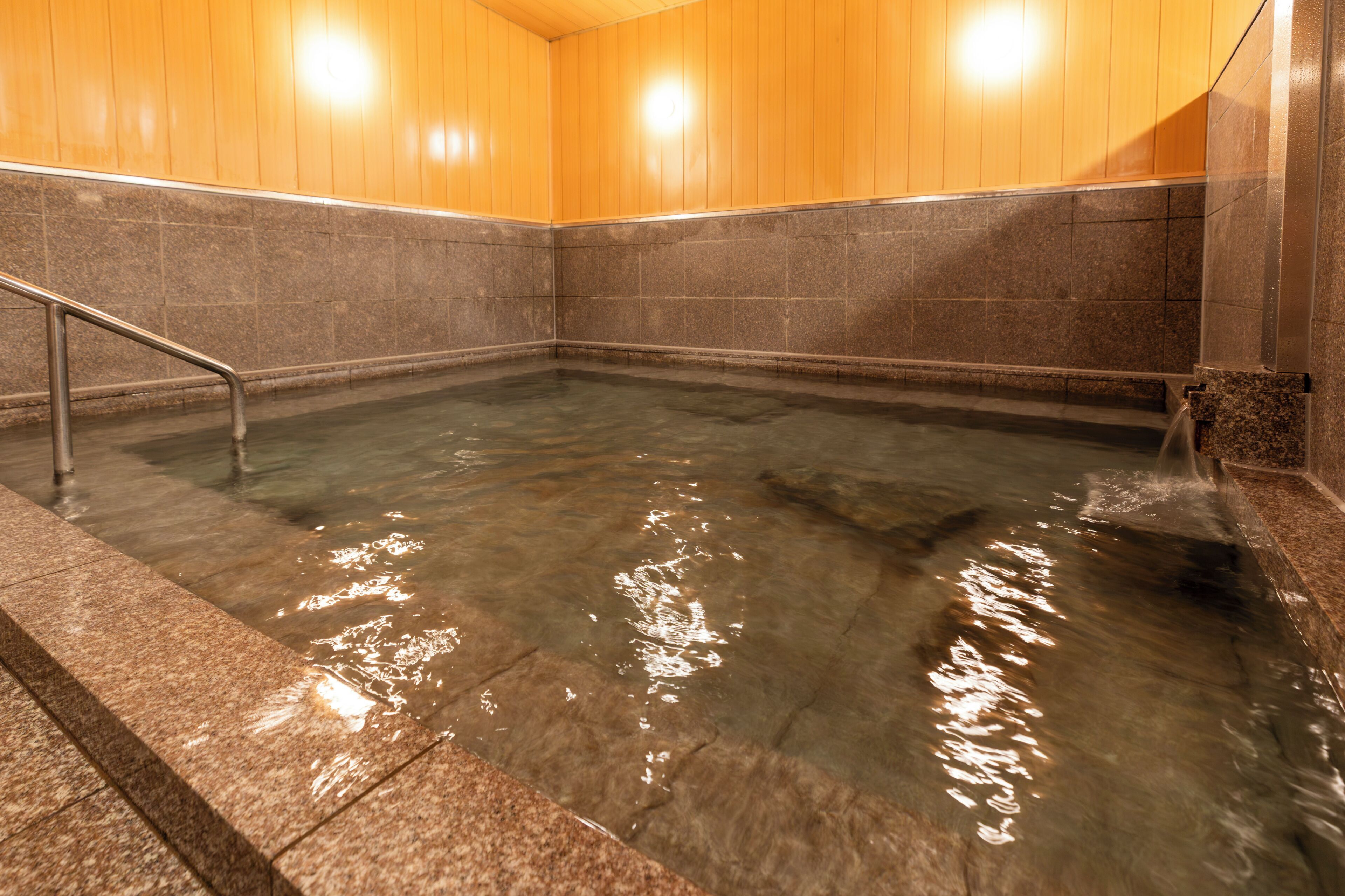A hot spring bath with a wooden ceiling and stone walls.