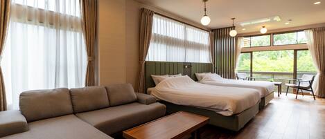 Una habitación de hotel con sofá, dos camas, una mesa de madera y ventanas amplias con cortinas.