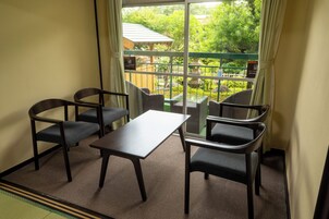 A room with a table and four chairs, a window with a view of greenery and a building outside.