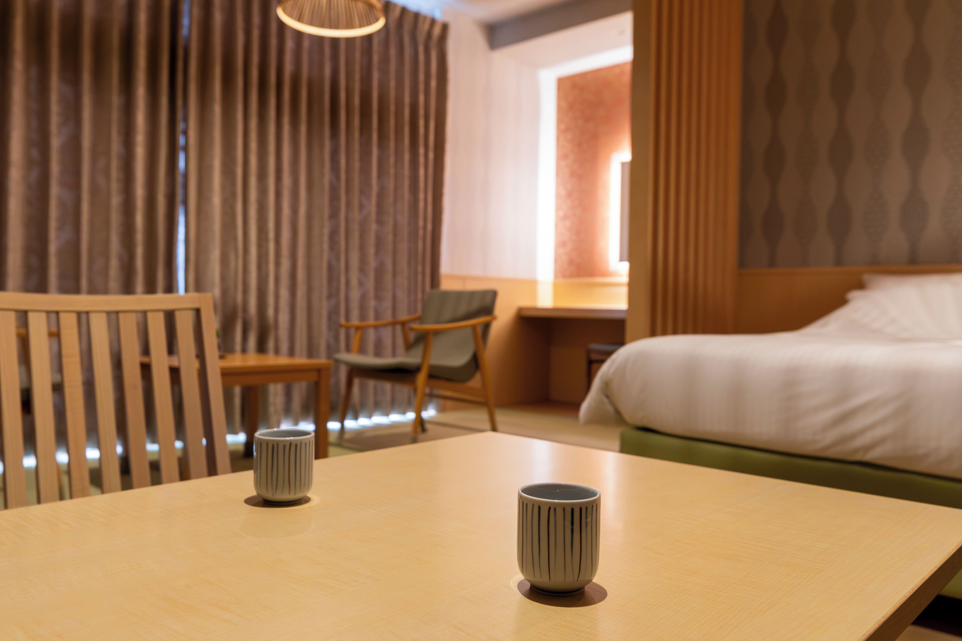 Una habitación de hotel con una cama, un escritorio, una silla y dos tazas sobre una mesa.