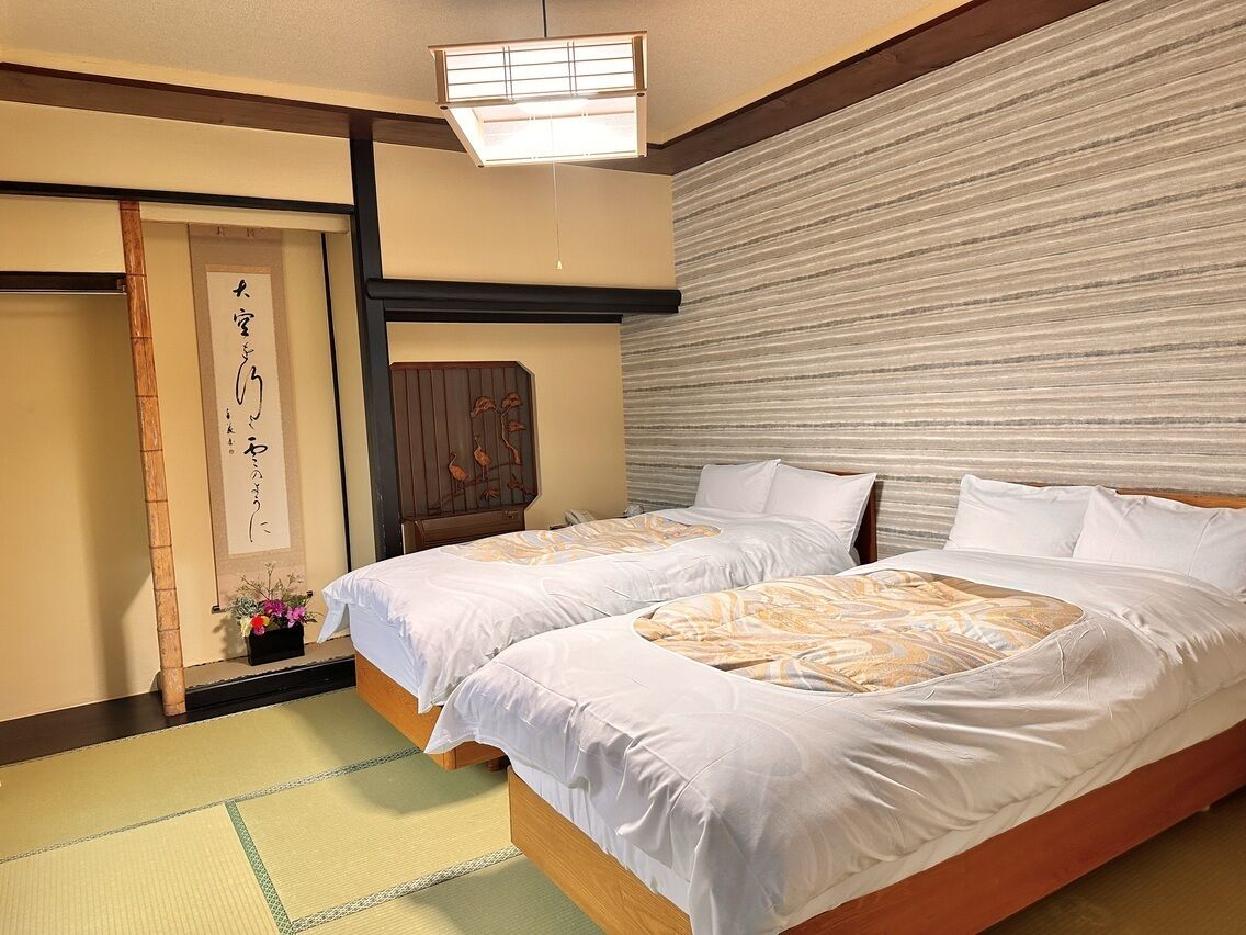 A traditional Japanese hotel room with tatami flooring, a shoji screen, and a futon bed.