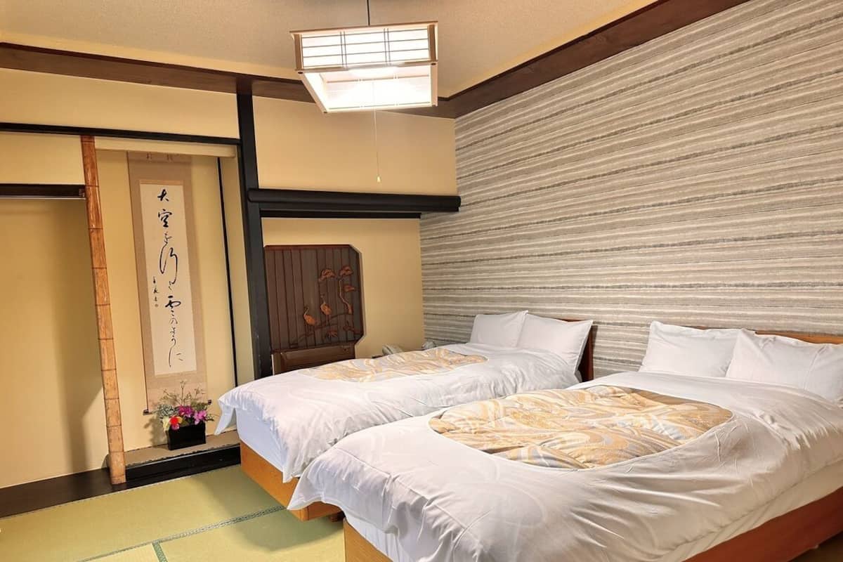 A traditional Japanese hotel room with tatami flooring, a shoji screen, and a futon bed.