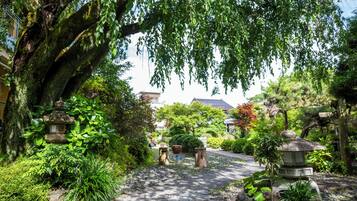 Um caminho serpenteia por um jardim com lanternas de pedra e uma grande árvore.