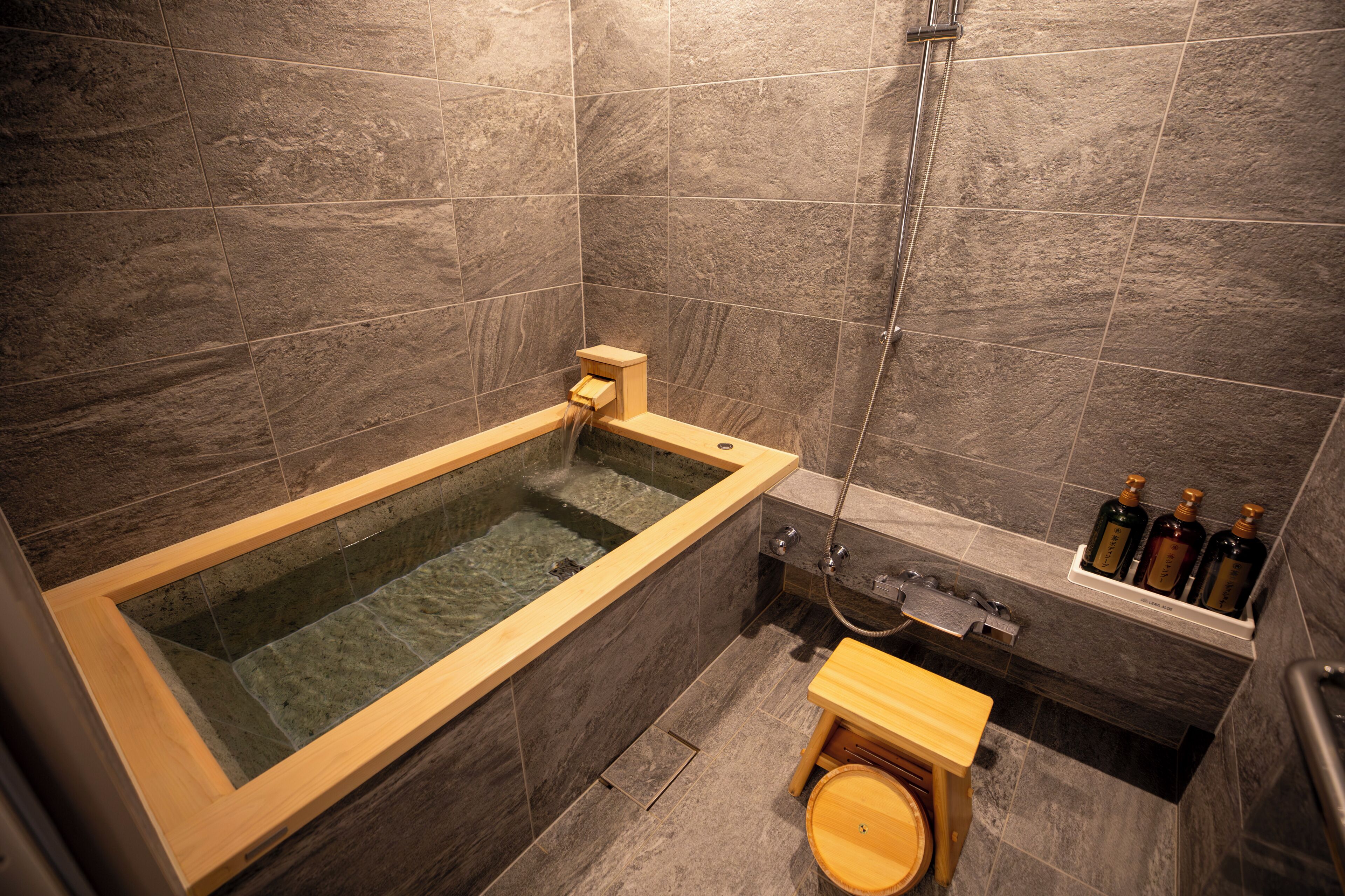 Un baño moderno con una bañera de madera, una zona de ducha y un taburete pequeño de madera.