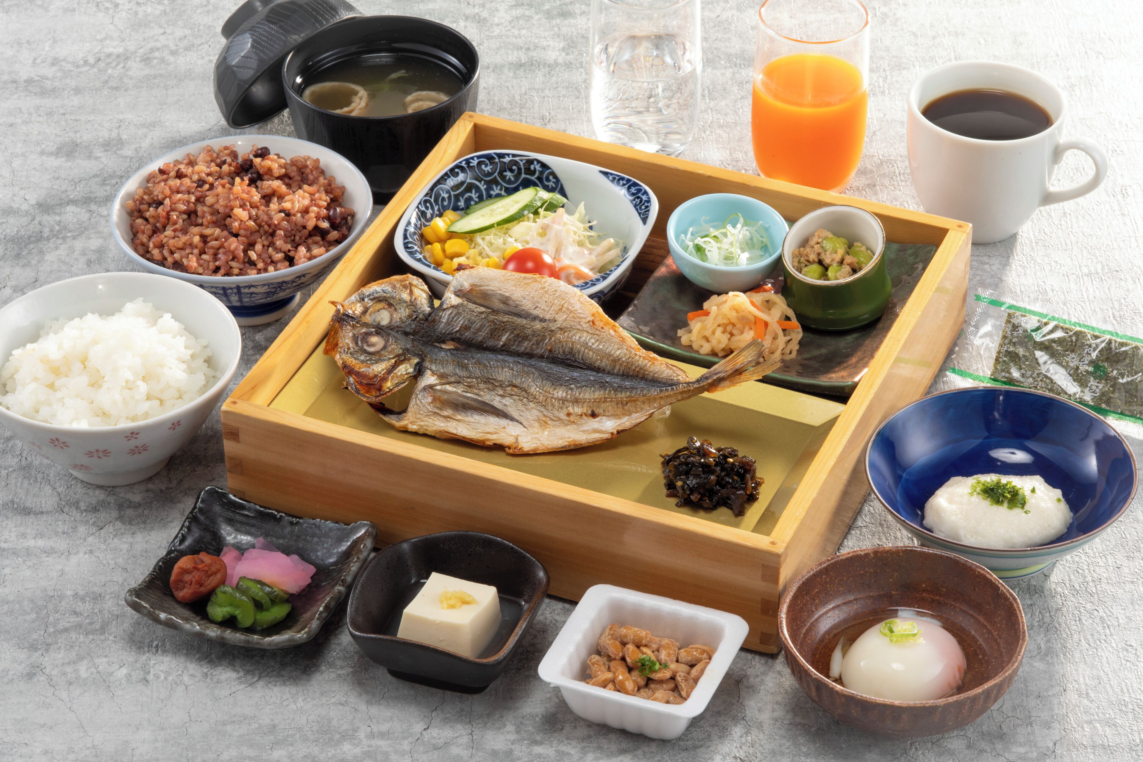 Verschiedene japanische Gerichte, darunter Reis, Fisch und eingelegtes Gemüse, auf einem Holztablett serviert.