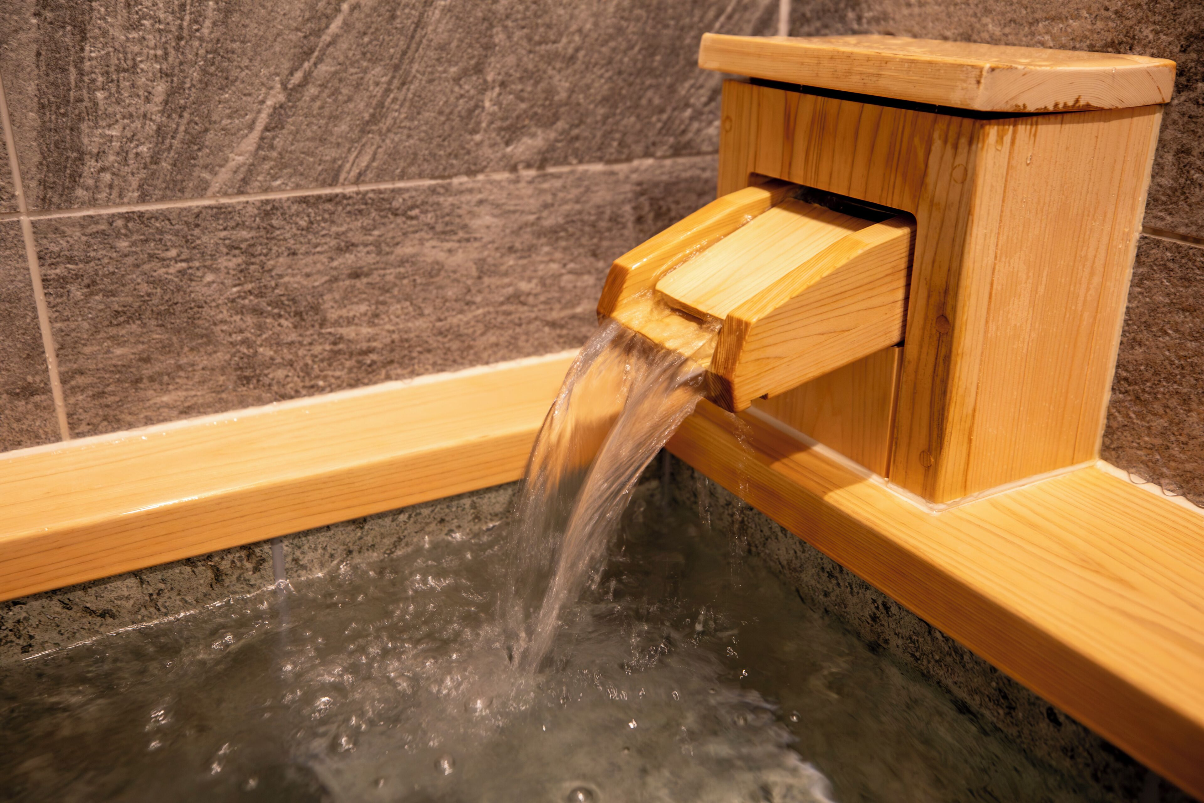 Une baignoire en bois avec un robinet en bois et un mur carrelé en arrière-plan.