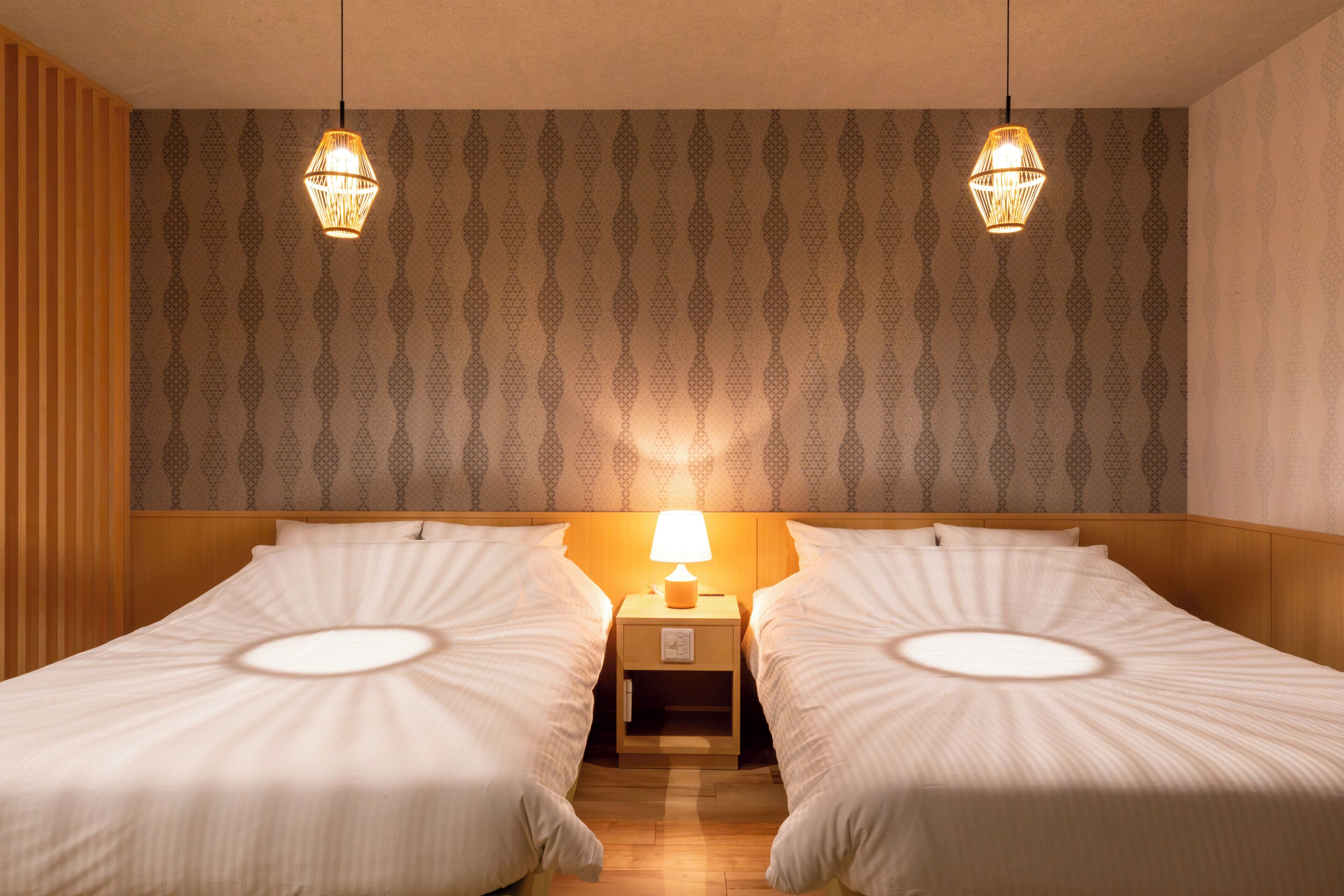 A hotel room with two single beds, a nightstand with a lamp, and patterned wallpaper.