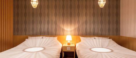 Habitación de hotel con dos camas individuales, una mesita de noche con lámpara y papel tapiz estampado.