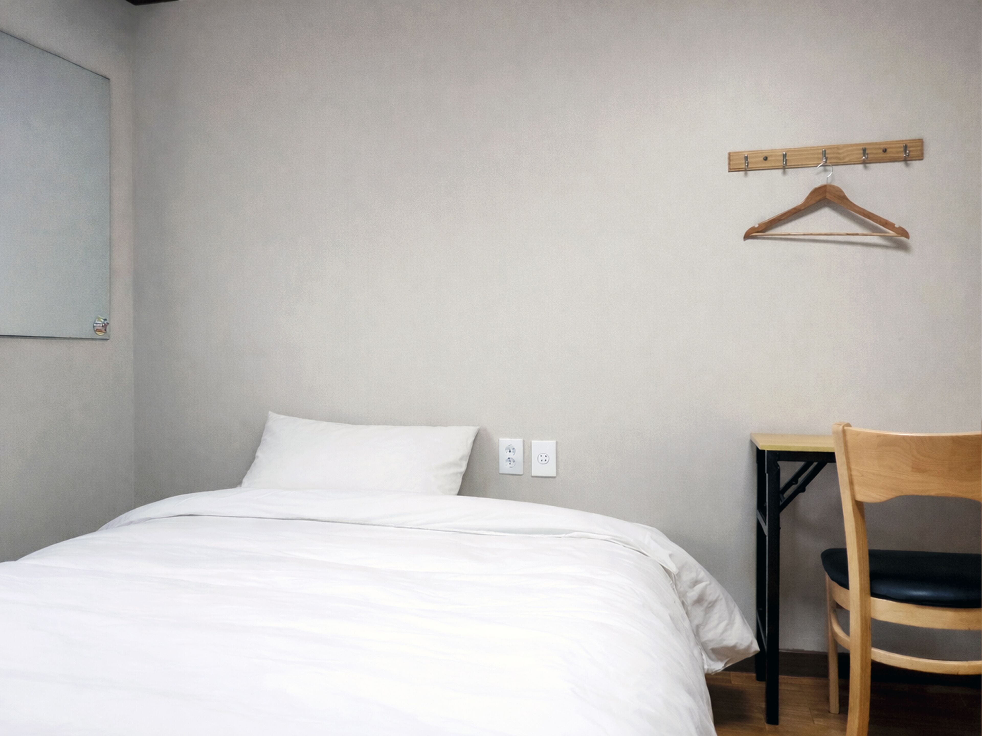 A bedroom with a bed, a chair, a coat rack, and a wall socket.
