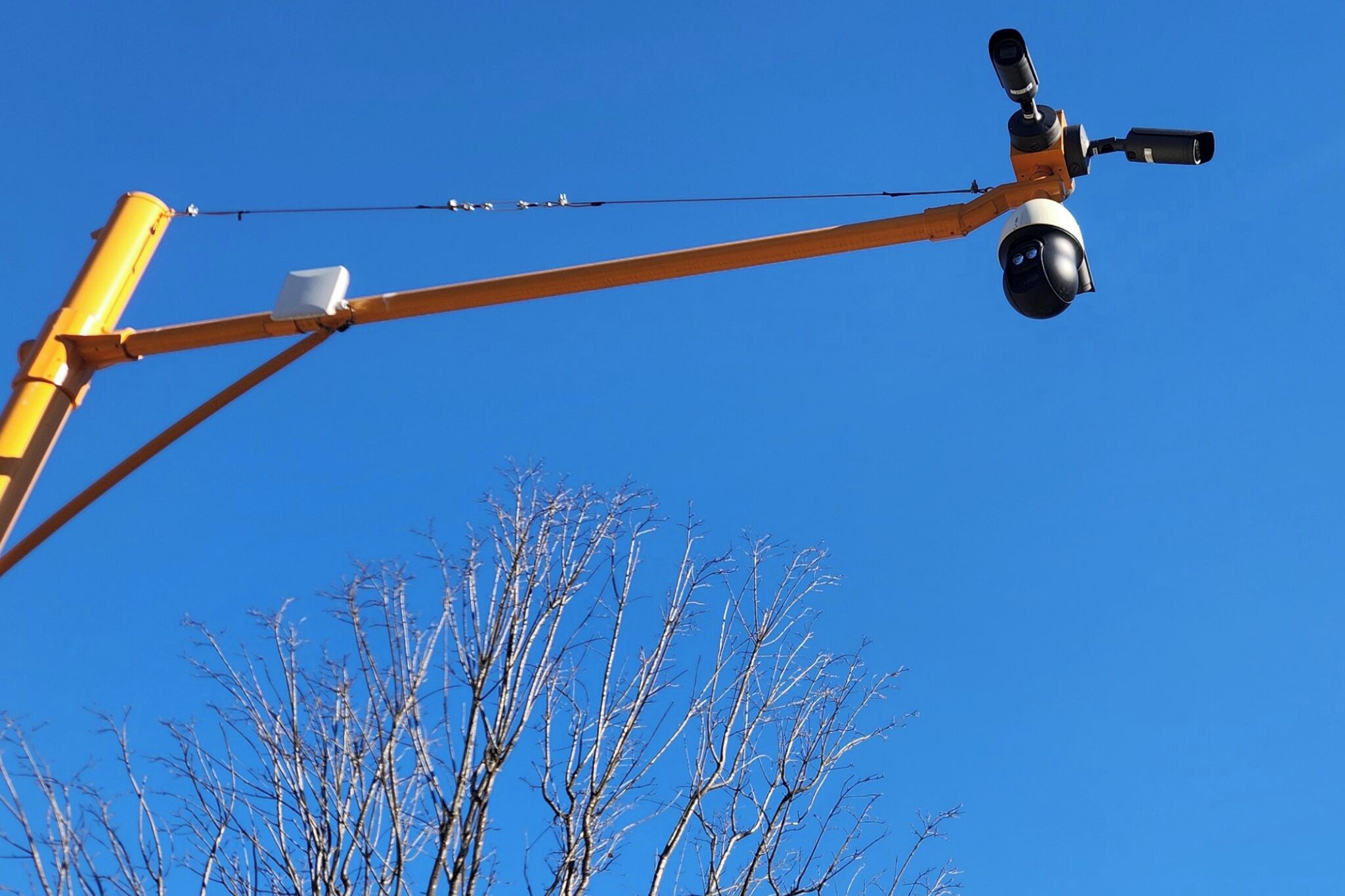 Une caméra de surveillance est fixée sur une structure métallique jaune, avec un ciel bleu clair en arrière-plan.
