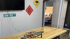 Ein langer Holztresen mit einem Logo, umgeben von Barhocker. An der Wand befinden sich Verkehrsschilder, darunter ein Schild mit der Aufschrift 'Road Work Ahead?' und ein Schild mit der Aufschrift 'Beer'.