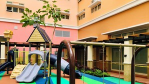 A playground with slides and swings, surrounded by a building with a pink facade.