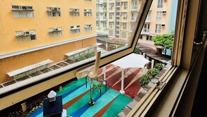 A view from a window of a multi-story residential building with balconies, a small outdoor seating area with a table and chairs, and a colorful mat on the floor.
