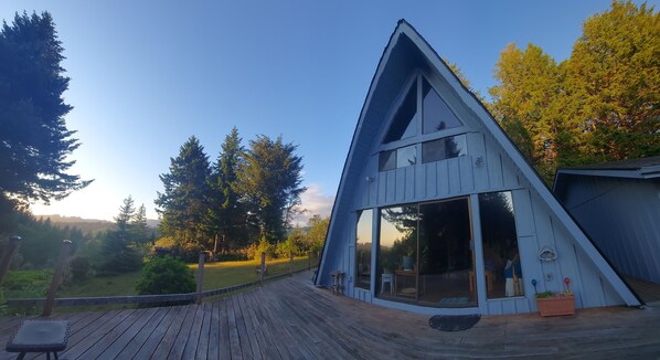 A modern, triangular wooden cabin with large sliding glass doors, a deck, and a view of a forested area. - Cozy Cabin with Sauna - Deja Vu (Brookings)