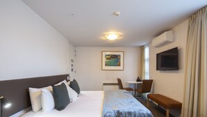 Habitación de hotel con cama, mesita de noche, escritorio, silla, banco, televisión y aire acondicionado.