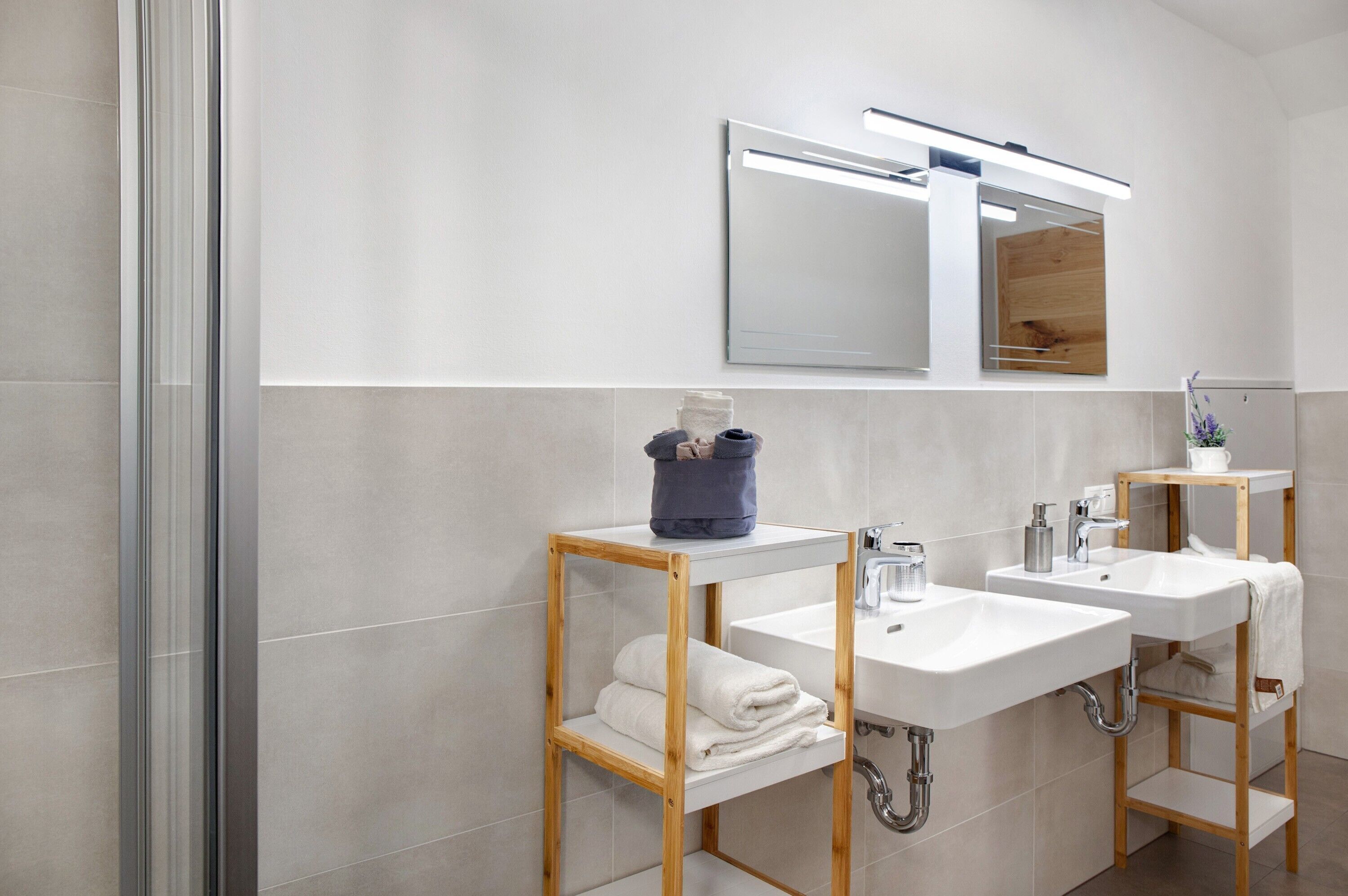 Een moderne badkamer met twee wasbakken, een spiegel en een douche.