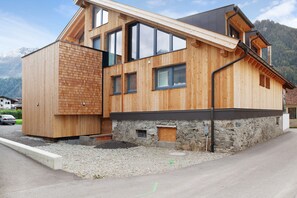 A modern wooden house with a stone foundation, large windows, and a sloped roof. - Apartment 'Bens Auszeit Top 5' with Mountain View and Wi-Fi (Umhausen)