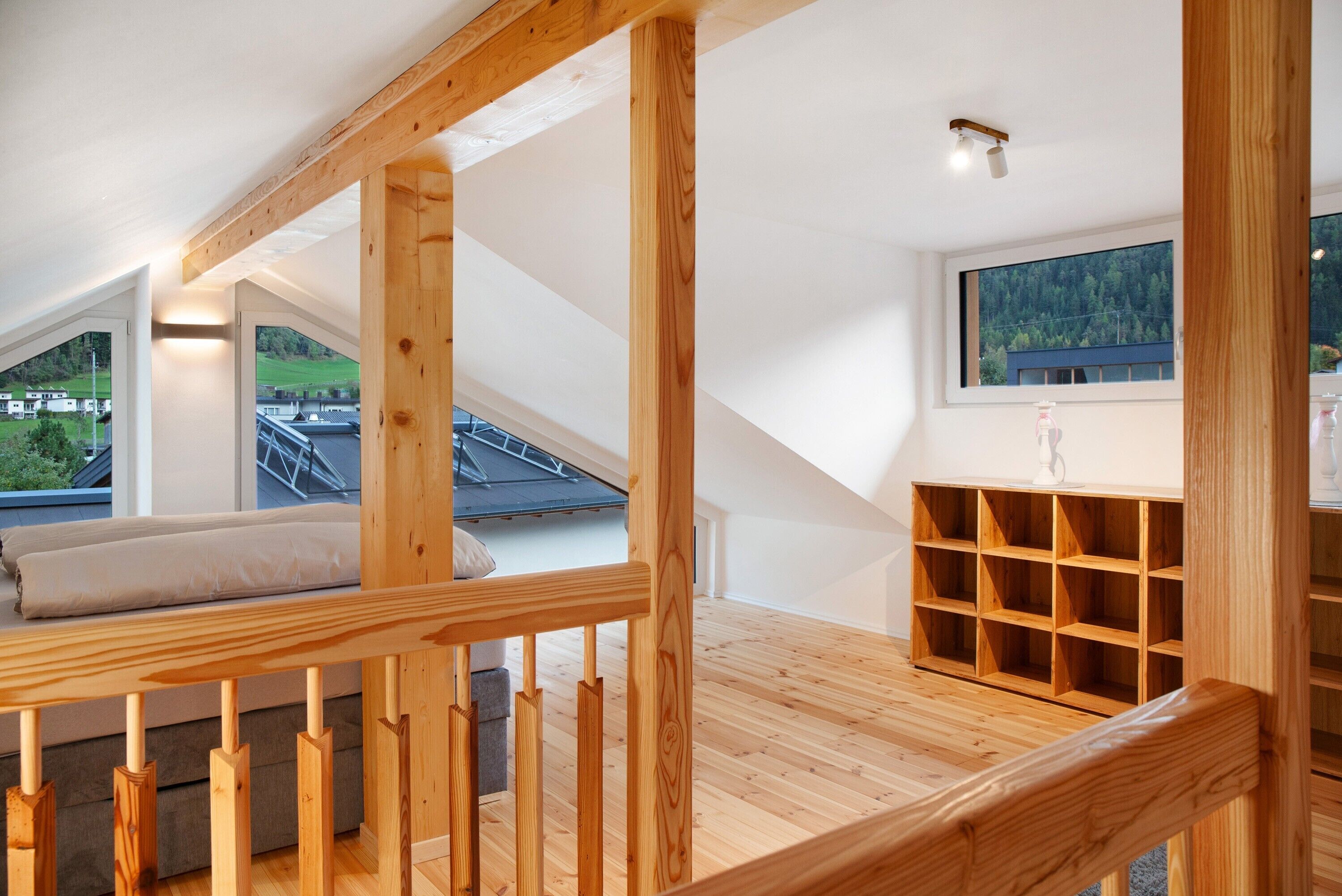 A wooden staircase leading to a loft bedroom with a view of a green landscape.