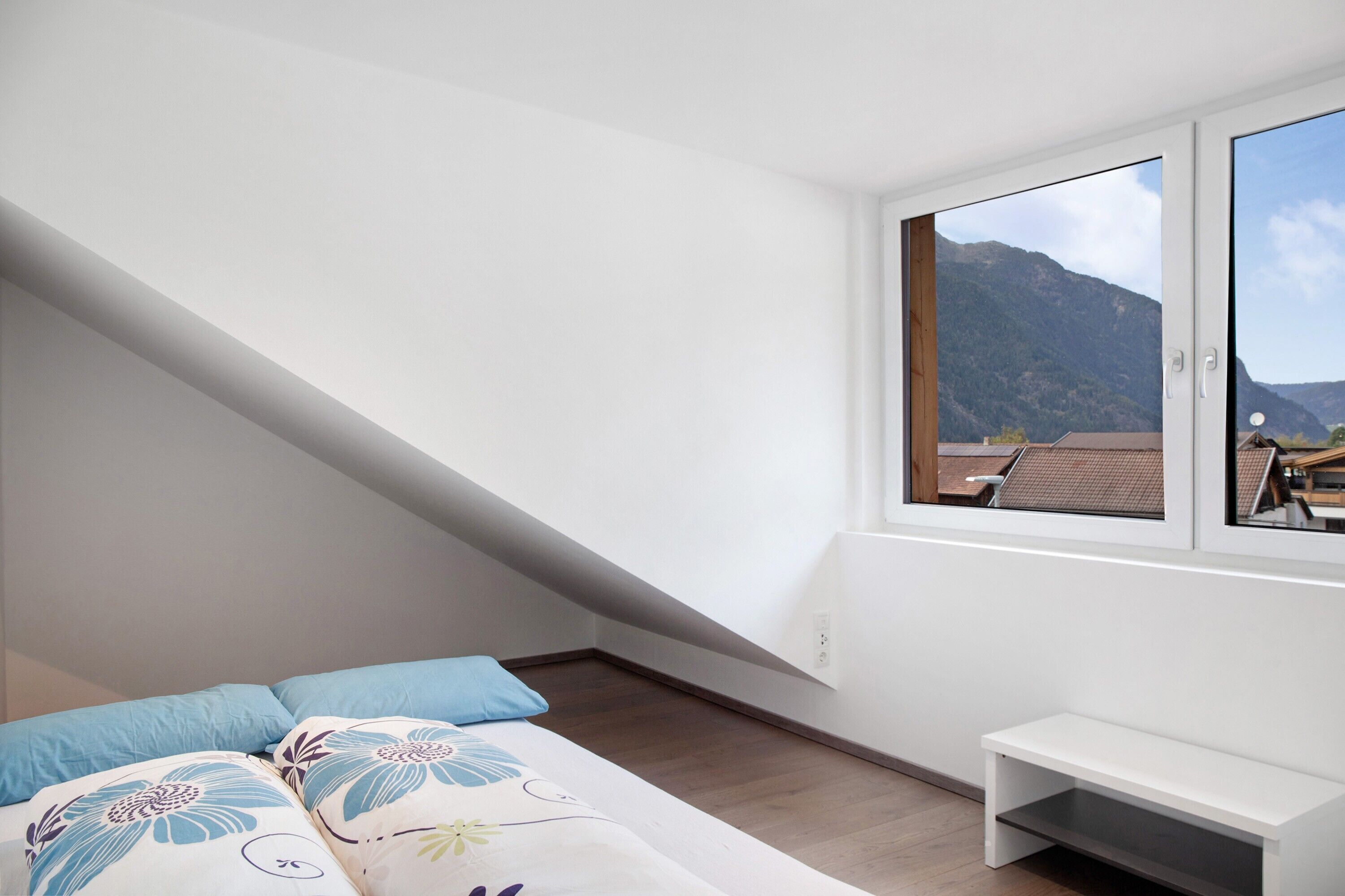 Een slaapkamer met een bed, kussens, een bankje en een raam met uitzicht op de bergen.