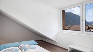 Een slaapkamer met een bed, kussens, een bankje en een raam met uitzicht op de bergen.
