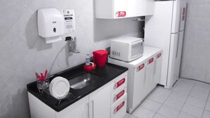 A modern kitchen with white cabinets, a black countertop, a microwave, and a refrigerator. - Hostel Kaizen (Curitiba)