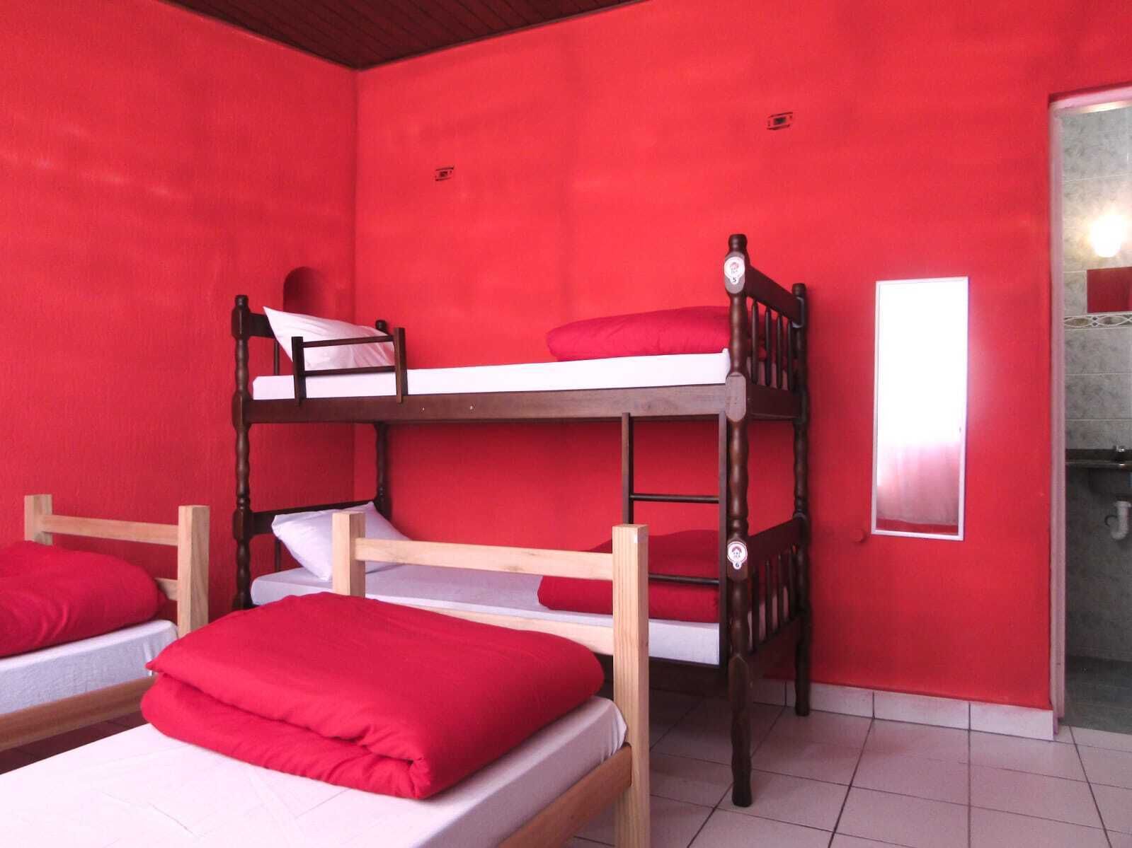 Une chambre avec deux lits superposés, des murs rouges et une petite fenêtre.