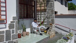 A man sitting on a chair on a stone staircase outside a building with a red railing, potted plants, and a window with a red grid pattern. - Hostel Kaizen (Curitiba)