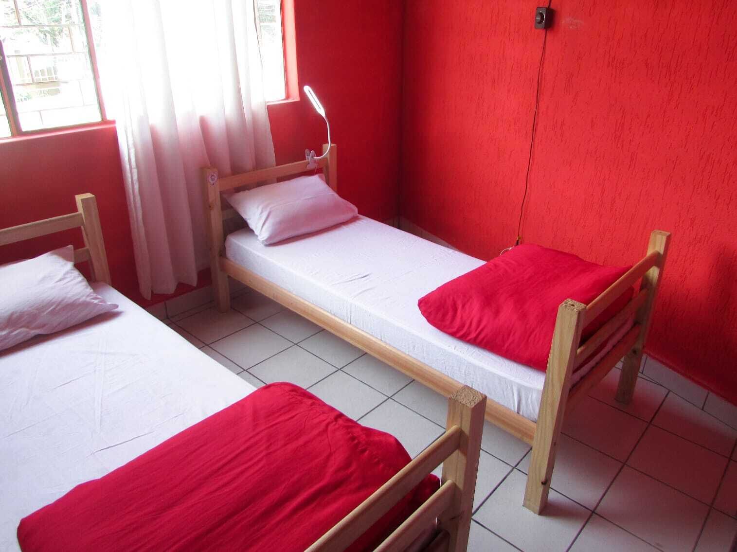 Une chambre de dortoir avec deux lits superposés en bois, chacun étant équipé d’un matelas blanc et de draps rouges.