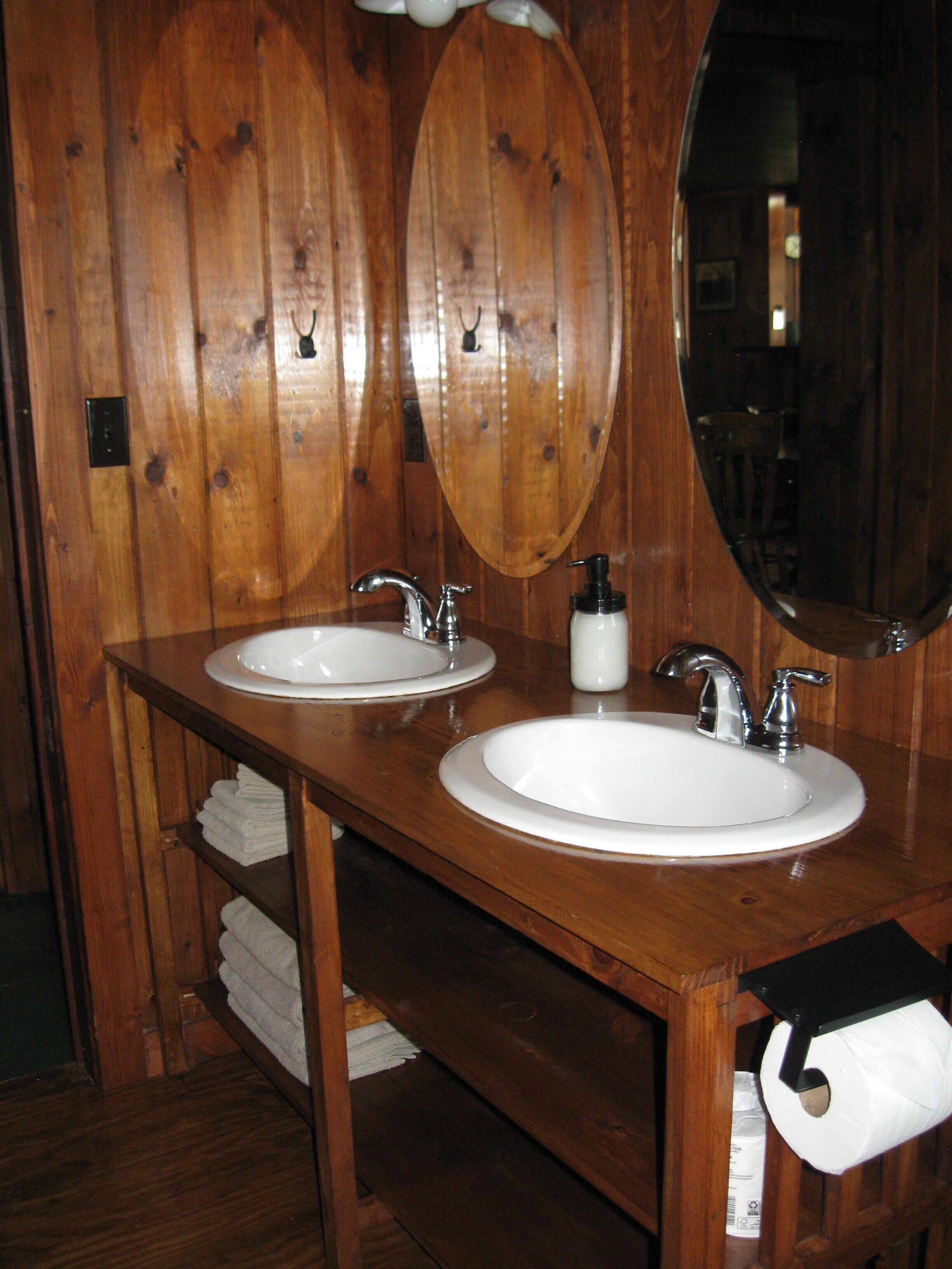 A wooden bathroom with two sinks, a mirror, and a toilet paper holder.