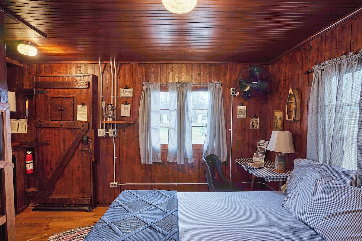 A wooden cabin room with a bed, a desk, and a chair.